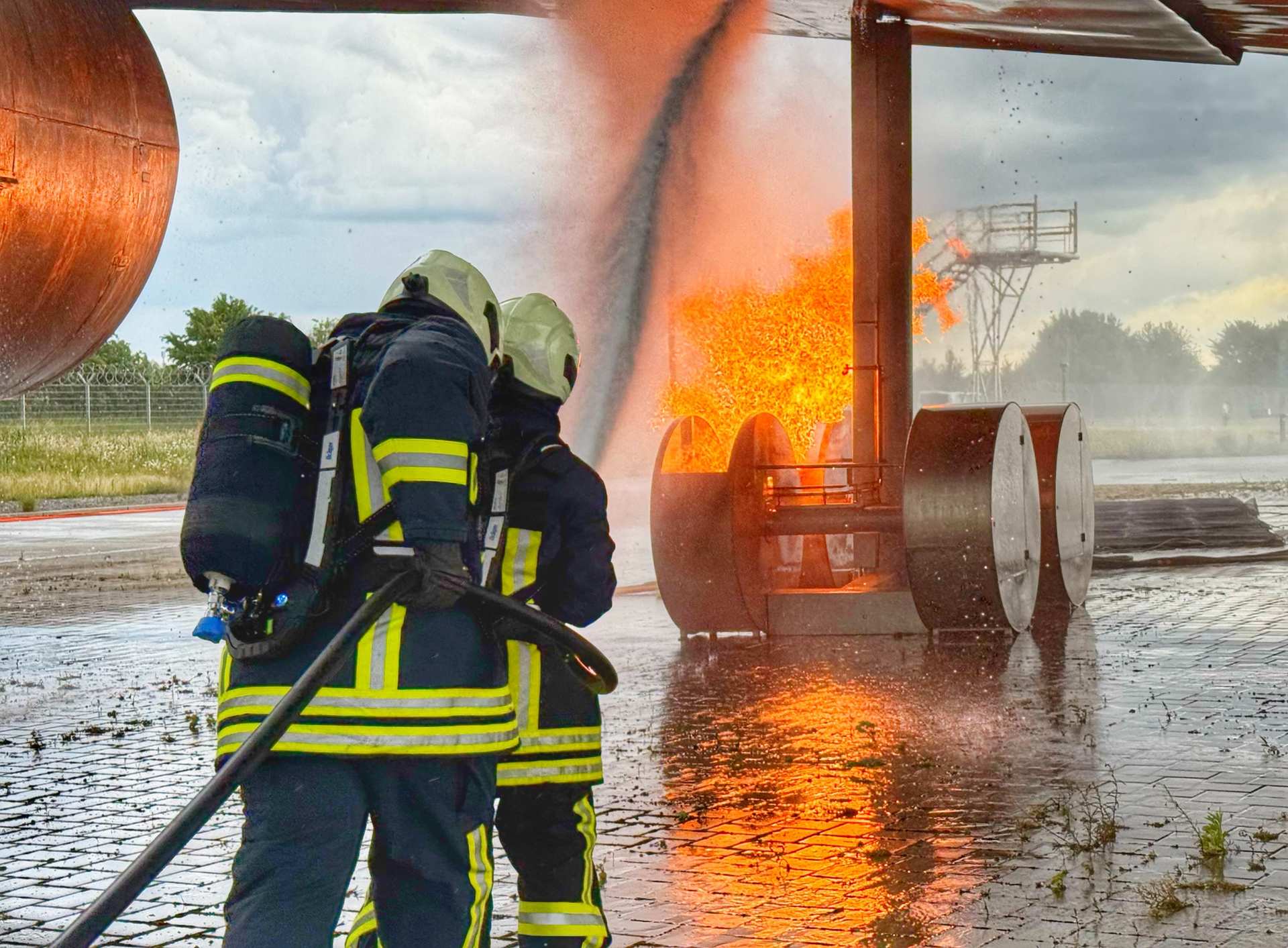 Flughafenfeuerwehr Grundausbildung (Initial Training) Zwei Feuerwehrleute in Vollschutz führen ein Strahlrohr am Brandherd
